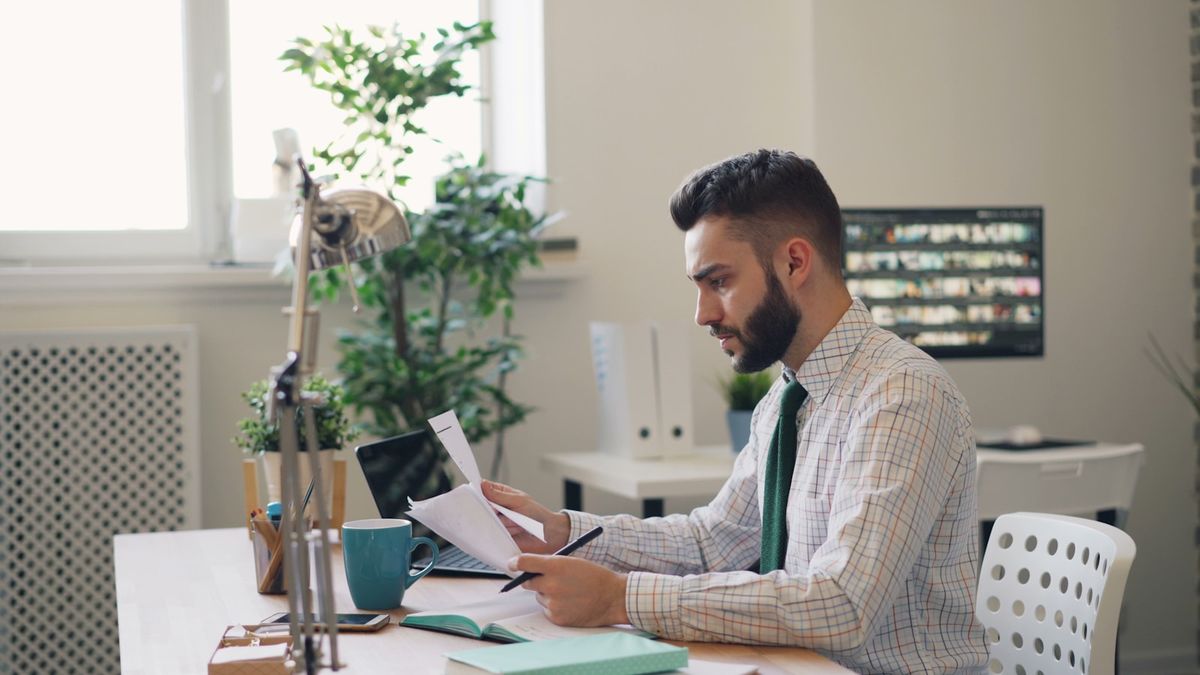 Person ved skrivebord med laptop og fakturapapirer